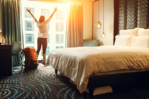 Opção de hospedagem barata com Hotéis Promo da 123milhas | Pessoa feliz no quarto de hotel | Conexão123