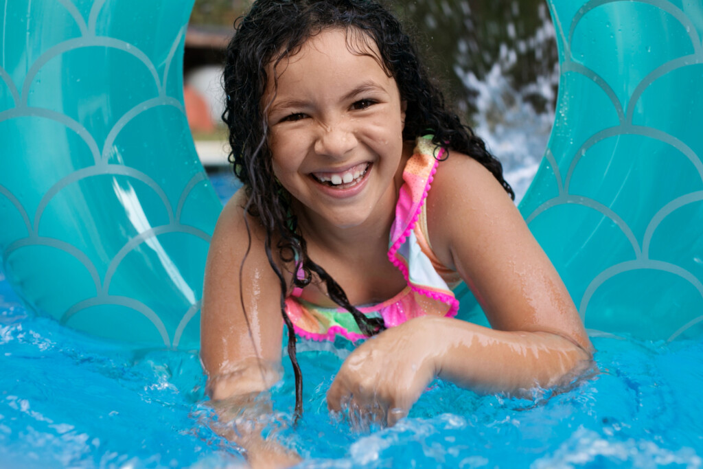 Férias de julho: conheça 3 destinos para viajar com as crianças | Criança se divertindo em piscina em cima de uma boia | Conexão123