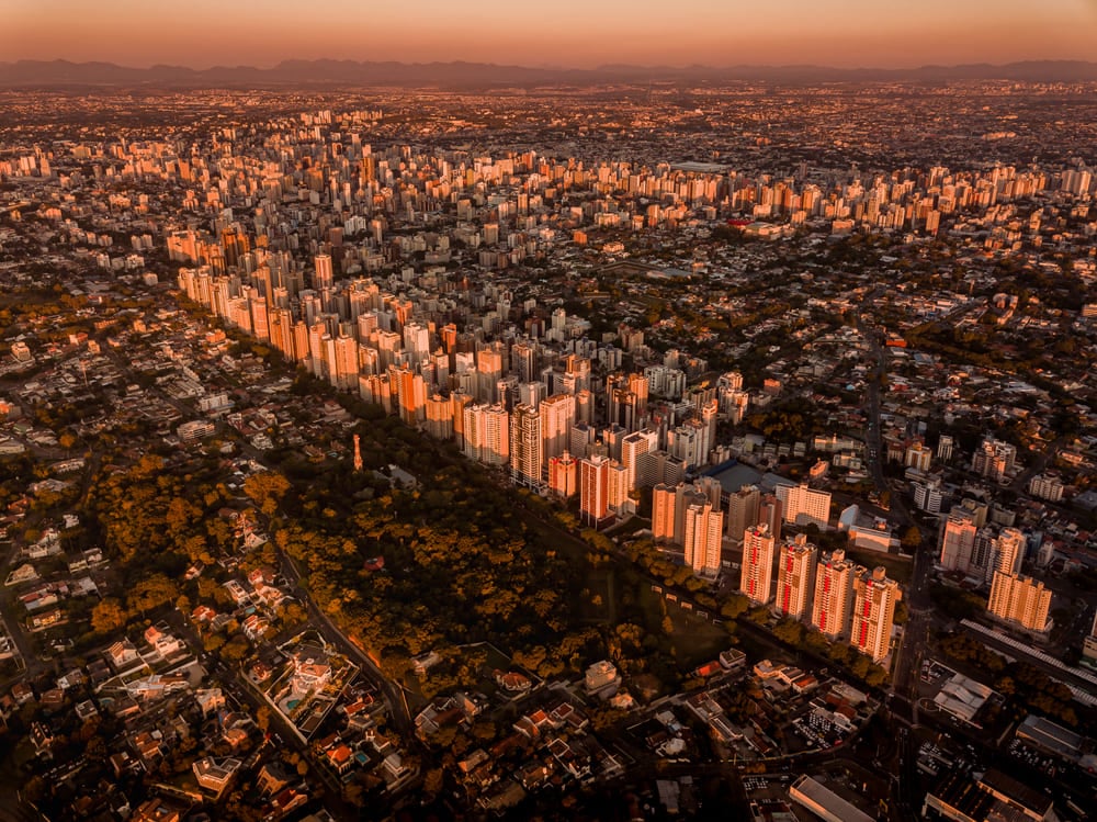 Celebrando o aniversário de Curitiba: quatro curiosidades sobre a cidade | Vista aérea da cidade de Curitiba (PR) ao entardecer | Conexão123