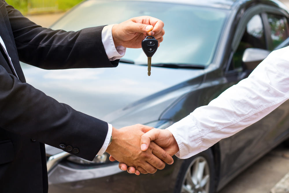 Cinco erros que comprometem uma viagem com carro alugado | Homem entregando as chaves do carro ao cliente e apertando as mãos | Conexão123