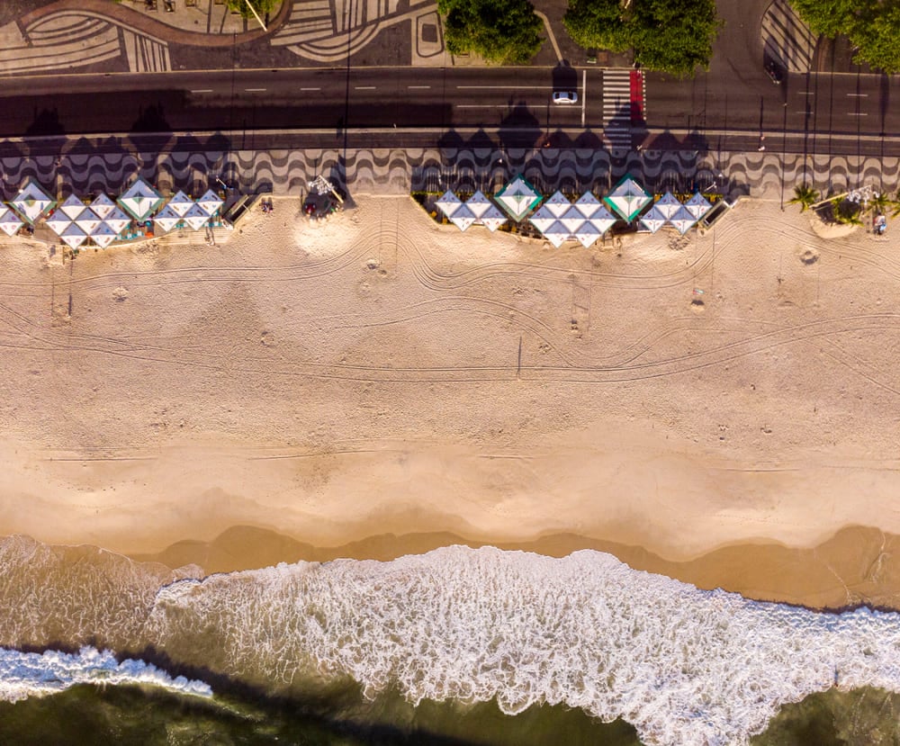 Viva o melhor do Rio de Janeiro com quatro experiências únicas | Vista de cima para baixo da praia de Copacabana com os quiosques no calçadão e as ondas chegando ao nascer do sol | Conexão123