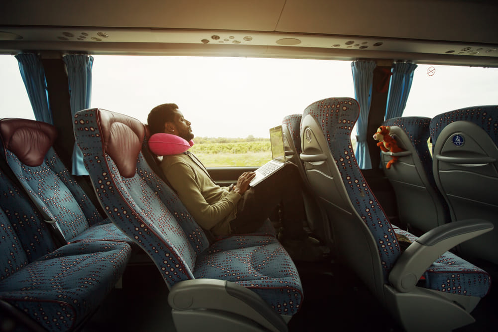Seis dicas para realizar uma viagem de ônibus | homem sorridente usando um laptop em uma viagem de ônibus | Conexão123