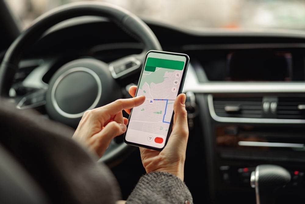 Cinco erros que comprometem uma viagem com carro alugado | Mulher usando o celular com o aplicativo de navegação GPS na tela enquanto está sentada no carro | Conexão123