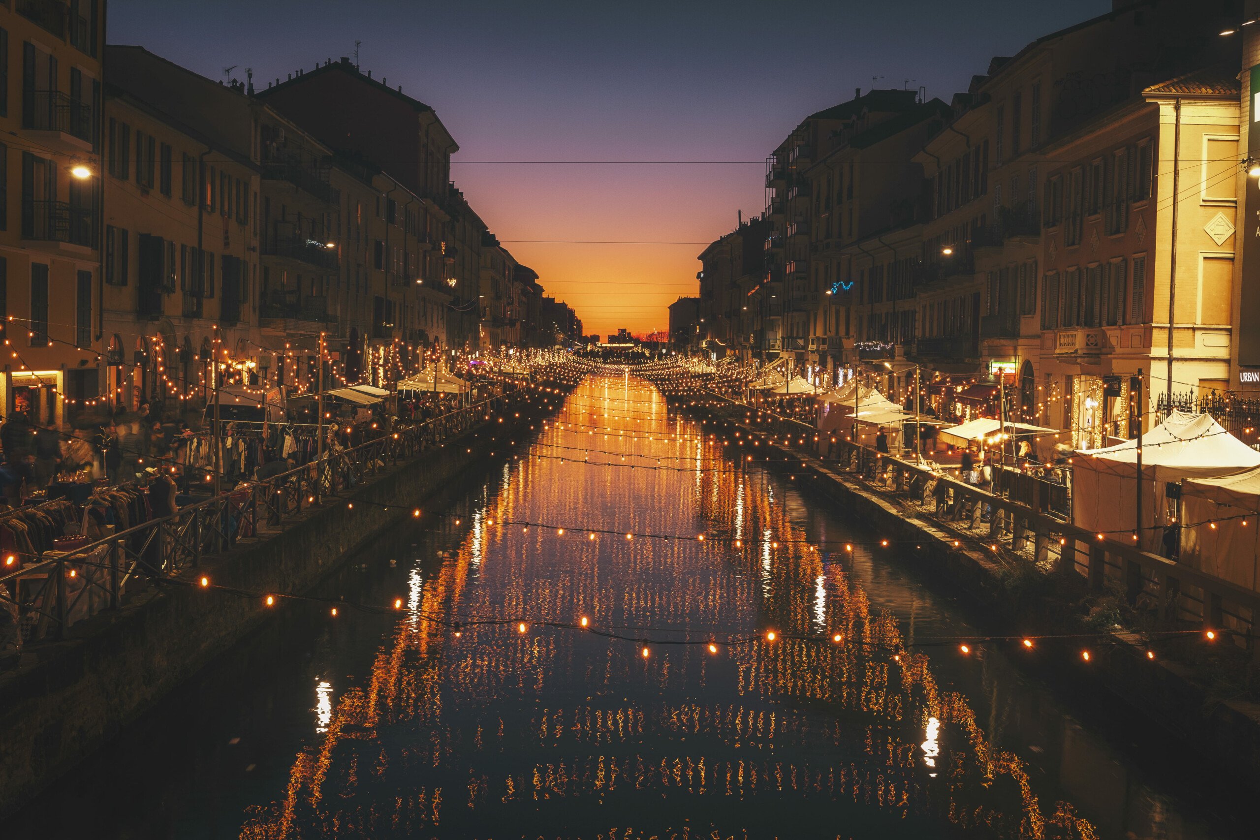 Turismo em Milão | Canal Navigli no bairro navigli sob a luz de luzes penduradas | Conexão123