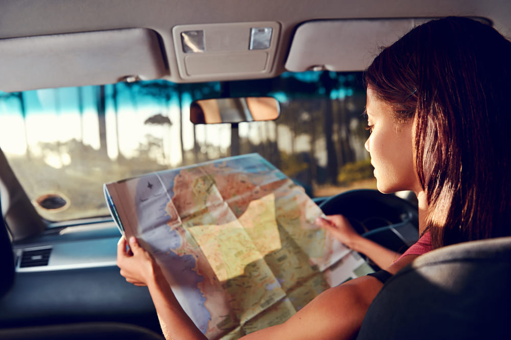 Vale a pena alugar um carro para viajar? | Moça dentro do carro com os pés para cima segurando um mapa | Conexão123