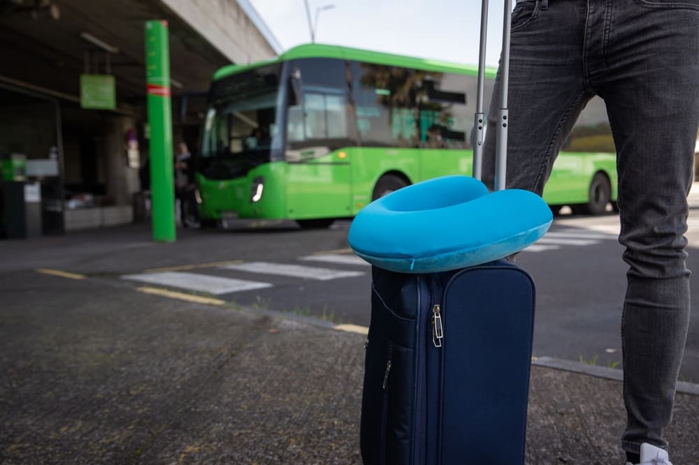 Aproveite os feriados para viajar de ônibus com conforto e segurança | Detalhe da mala de um viajante com o travesseiro de viagem na estação rodoviária | Conexão123