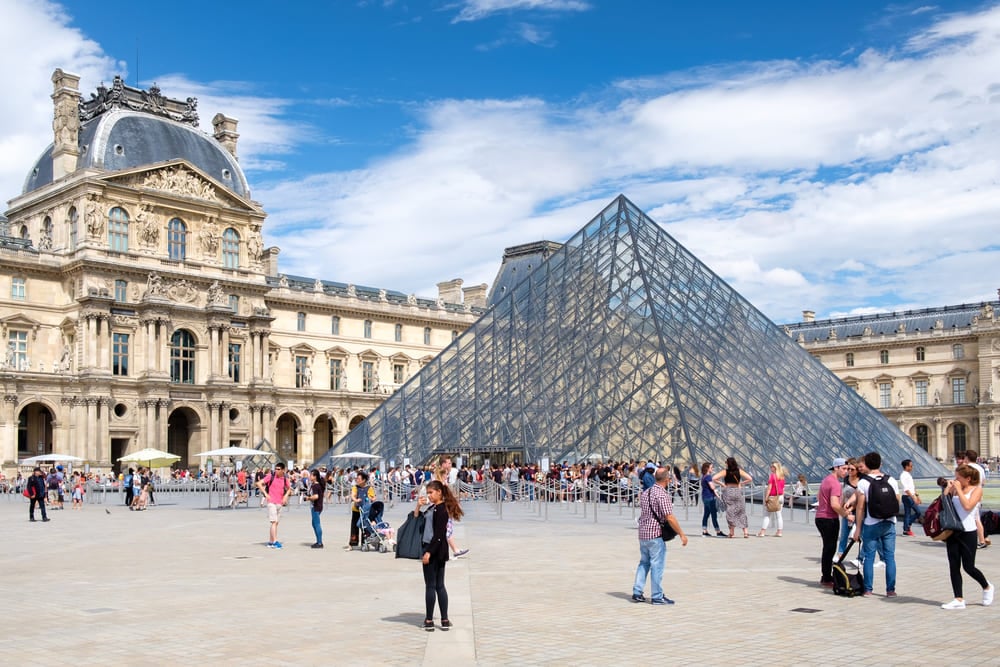 Turismo em Paris: guia de viagem | Imagem do Museu do Louvre em Paris, França, com sua famosa pirâmide de vidro no centro do pátio | Conexão123