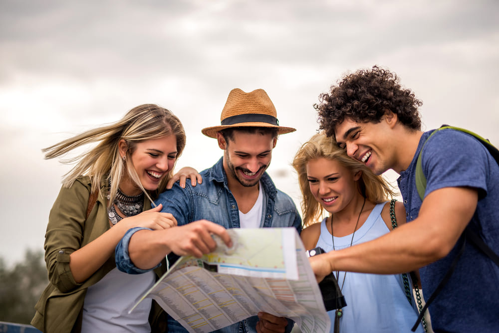 Roteiro de viagem eficiente: cinco dicas para torná-lo mais enxuto | Grupo de amigos viajando olhando mapa | Conexão123