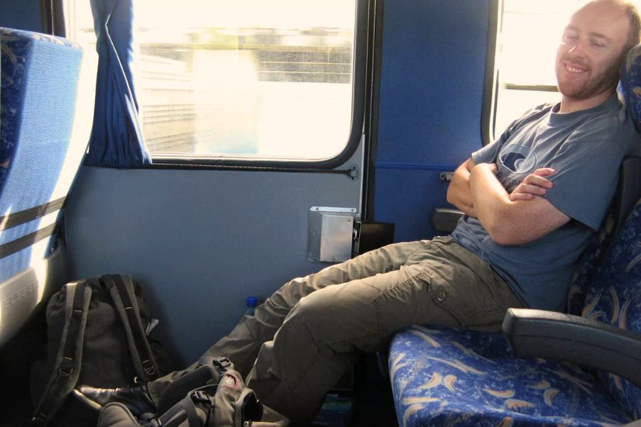 Cuidados com a coluna em viagens longas: cuide-se com cinco dicas | Homem em uma viagem de ônibus esticado em sua poltrona | Conexão123